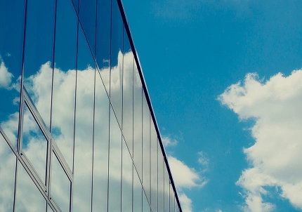 Blue sky with white clouds reflected on the glass windows of a modern building, emphasizing clarity and reflectivity.