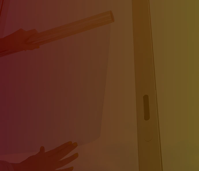 Dimly lit image of a person applying a sheet of window film to a tall glass window, partially obscured by a dark red and yellow overlay.